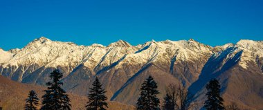 Karla kaplı dağ zirveleri. Yamaçlarda sonbahar ormanı