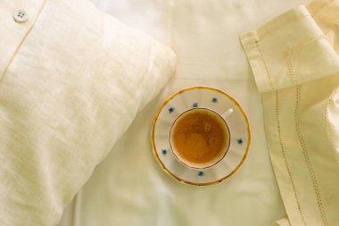 Beyaz çarşafta bir fincan kahve. Yatakta kahve. Düz yatıyordu