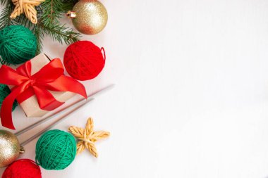 Noel kompozisyonu. Kırmızı ve yeşil iplik yumakları, beyaz arka planda kırmızı kurdeleli hediyeler. Parlak iplik örme konsepti. Düz yatış, üst görünüm.