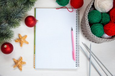 Gri bir sepetteki yeşil ve kırmızı iplik, notlar için bir defter, örgü iğneleri ve beyaz arka planda bir ladin dalı. Ev konforu ve Noel konsepti. Kadın ve erkeğin hobisi örgü örmektir..