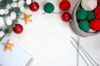 Gri bir sepetteki yeşil ve kırmızı iplik, notlar için bir defter, örgü iğneleri ve beyaz arka planda bir ladin dalı. Ev konforu ve Noel konsepti. Kadın ve erkeğin hobisi örgü örmektir..