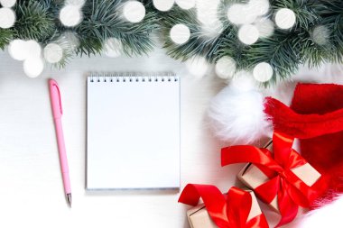 Noel hediyeleri, bir köknar dalı ve beyaz arka plan notları için bir defter. Mutlu Noeller ve Mutlu Noeller kartpostalları, çerçeve. Kış Noel teması. Düz yatış, üst görünüm.