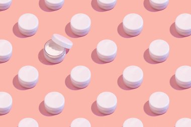 Pastel pembe arka planda kapalı krema kalıpları. En düşük cilt bakımı konsepti.