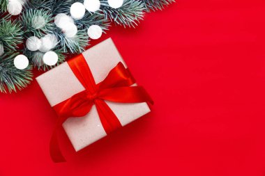 Noel fiyonklu bir hediye kutusu ve kırmızı arka planda bir köknar dalı ve fotokopi alanı. Yeni yıl kompozisyonu. Düz yerde, üst tarafta. Asgari biçim.