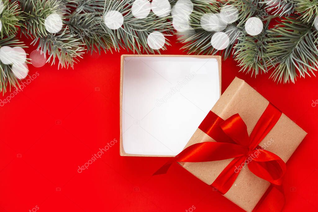 Open gift box with Christmas bow and fir branch on red background with copy space. New Year composition. Flat lay, top view. Minimalistic style.