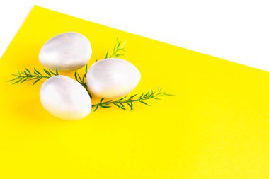 Paskalya bayramı kompozisyonu. Çift sarı-beyaz arka planda yeşil bir dal ile üç gümüş renkli yumurta. Paskalya usulü ley. Paskalya konsepti. Kopyalama alanı.