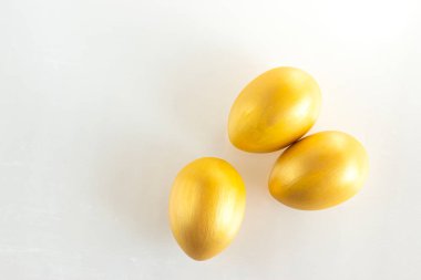 Beyaz arka planda üç altın rengi yumurta. Minimalist kompozisyon. Paskalya bayramı kartı.