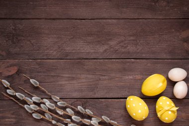 Paskalya bayramı kartı. Sarı boyalı yumurtalar, söğüt dalları koyu ahşap bir masada. Metin için alanı kopyala.
