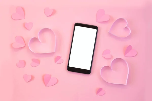 Paper cut hearts, mobile phone on pastel pink background. Composition for Valentine's Day, postcard. Flat lay, top view, copy space.