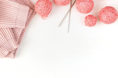 Pembe iplik derileri, metalik örgü iğneleri ve hafif arka planda örülmüş bir süveter. Kadın nakış işi konsepti. Düz yatıyordu.