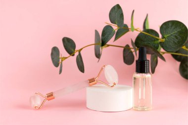 Yüz masajı için pembe kuvars silindiri ve pembe arka planda bir kavanoz kozmetik serumu. Güzellik ve cilt bakımı konsepti. Yaşlanma karşıtı terapi ve kaldırma.