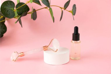 Yüz masajı için pembe kuvars silindiri ve pembe arka planda bir kavanoz kozmetik serumu. Güzellik ve cilt bakımı konsepti. Yaşlanma karşıtı terapi ve kaldırma.