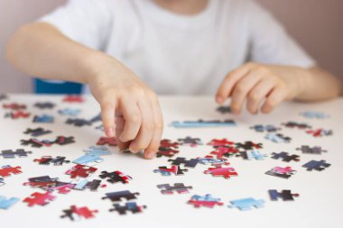 Çocuk bir bulmaca topluyor. Bulmacanın elementleri beyaz bir masanın üzerinde serili. Maç sırasında çocukların elleri. Ev eğlencesi..