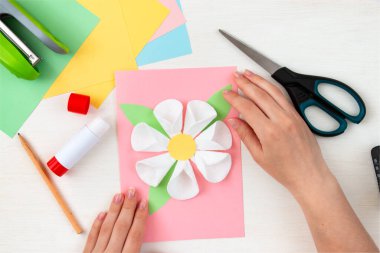 Pamuktan yapılmış bir çiçek. Renkli kağıt, zımba, makas, makas, beyaz masadaki kalem. Anneler günü için çocuk el işi kartı. Adım adım talimat veriyorum. 9. adım.