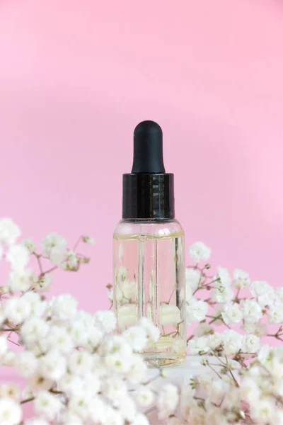 Cosmetic bottle with dropper on a pink background. Flowering branch of gypsophila. natural cosmetics concept and bernding.