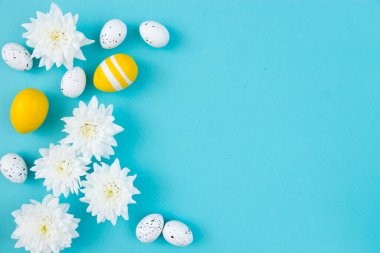Beyaz çiçekler ve mavi arka planda boyanmış Paskalya yumurtaları. Temiz metin alanı olan şenlikli çiçek konsepti. Düz yatıyordu. Yukarıdan görüntüle.