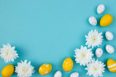 Beyaz çiçekler ve mavi arka planda boyanmış Paskalya yumurtaları. Temiz metin alanı olan şenlikli çiçek konsepti. Düz yatıyordu. Yukarıdan görüntüle.