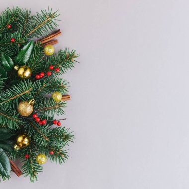 Ladin dalları, kırmızı böğürtlenler, tarçın çubukları ve altın topları olan bir Noel arkaplanı. Gri arka plan. Düz yatıyordu. Metin için yer.