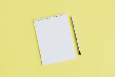 Sarı arka planda boş sayfa ve kalem olan defter. Düz yatıyordu. Metin için yer. 