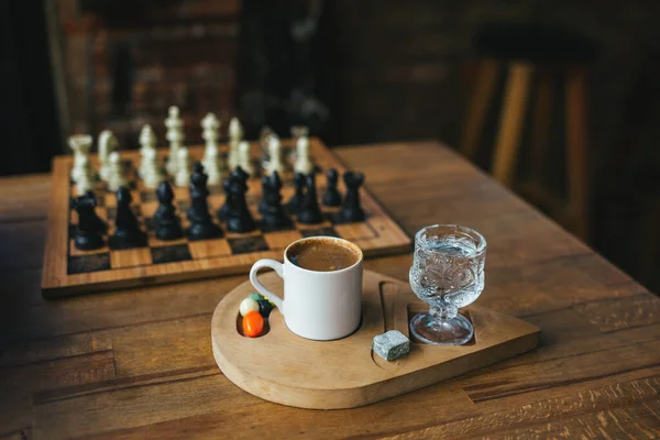 Cup of arabic coffee with a glass of water on a wooden table in a turkish cafe, Istanbul, Turkey. Old chess on background.