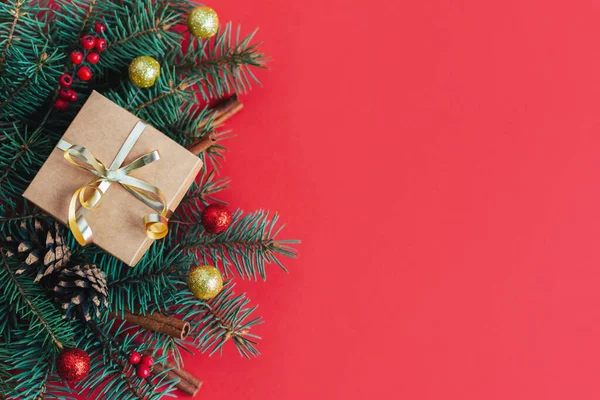 Ladin dalları, kırmızı böğürtlenler, koniler, tarçın çubukları ve hediye kutusuyla Noel arkaplanı. Tatil konsepti. Kırmızı arka plan. Metin için yer.