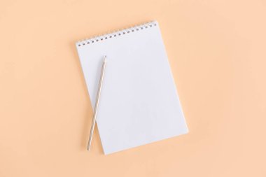 Şeftali rengi arka planda boş sayfa ve kalem olan defter. Düz yatıyordu. Metin için yer. 