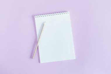 Menekşe rengi pastel arka planda boş sayfa ve kalem olan defter. Düz yatıyordu. Metin için yer. 