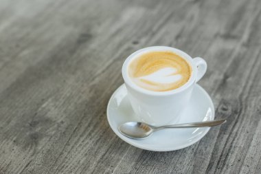 Kırsal ahşap masa üzerinde latte sanatıyla bir fincan kahve. Metin için yer.