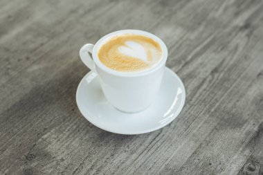 Kırsal ahşap masa üzerinde latte sanatıyla bir fincan kahve. Metin için yer.