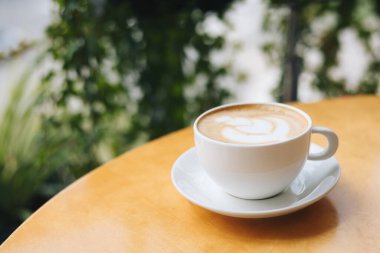 Kafedeki ahşap bir masanın üzerinde latte resimli bir fincan kahve. Metin için yer.