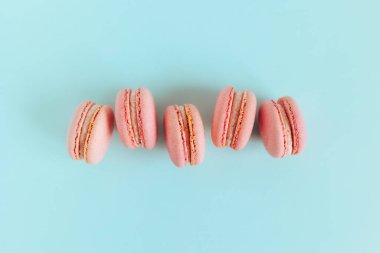 Mavi pastel arka planda lezzetli, pembe Fransız badem kurabiyeleri. Metin için yer.