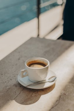Cup of black coffee on a table in a cafe by the sea in a sunlight. Selective focus. Place for text.