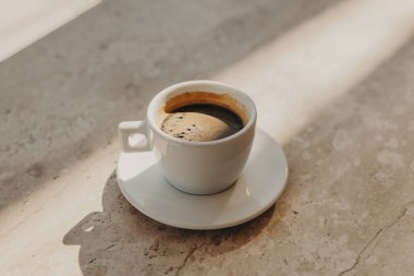 Güneş ışığında bir kafede mermer bir masanın üzerinde bir fincan sade kahve. Doğal sıcak renkler. Metin için yer.