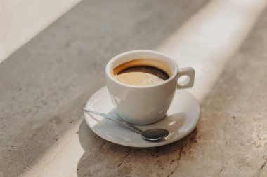 Güneş ışığında mermer bir masada bir fincan sade kahve. Doğal sıcak renkler. Metin için yer.