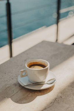 Deniz kenarındaki bir kafede, taştan bir masada güneş ışığında bir fincan sade kahve. Seçici odaklanma. Metin için yer.