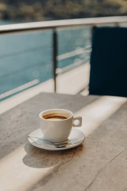 Deniz kenarındaki bir kafede, taş bir masanın üzerinde bir fincan sade kahve. Seçici odaklanma. Metin için yer.