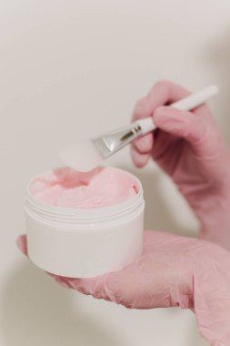 Beyaz kavanozda yüz maskesi ve kozmetik uzmanının ellerinde fırça. Cilt bakımı güzellik ürünü. Kozmetoloji kavramı.
