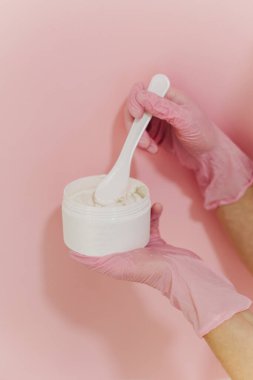 Beyaz kavanozda yüz maskesi ve pembe arka planda bir kozmetikçinin ellerinde fırça. Cilt bakımı güzellik ürünü. Kozmetoloji kavramı.