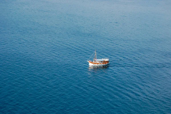 Sakin mavi deniz suyunda tek başına yüzen küçük geleneksel bir teknenin havadan görünüşü. Kopyalama alanı, barışçıl seyahat ve turizm konsepti olan minimalist deniz manzarası, yumuşak dalgalı berrak su yüzeyi, gün ışığı