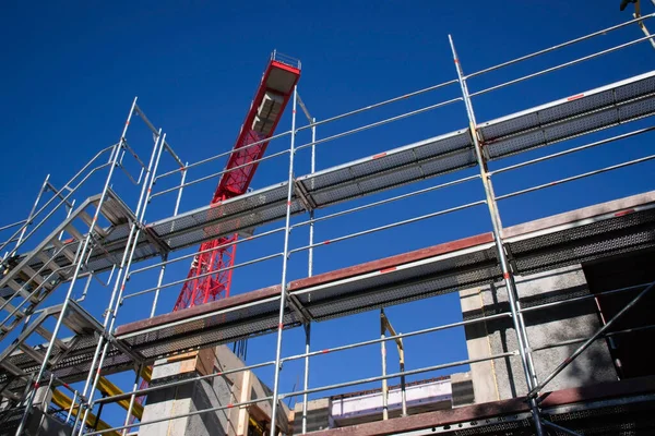 Metal iskelenin düşük açılı görüntüsü ve inşaat alanında açık mavi gökyüzüne karşı kırmızı kule vinci. Gelişim halindeki somut yapı, endüstriyel mimari ve kentsel yapı kavramı