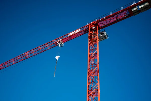 Derin mavi gökyüzüne karşı inşaat alanındaki kırmızı bir kule vincinin yakın görüntüsü. Kanca ve çelik kablo ile endüstriyel kaldırma ekipmanları, modern kentsel gelişim ve inşaat endüstrisi konsepti