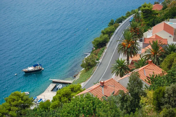 Palmiye ağaçları ve turkuaz deniz manzaralı evler olan kıyı yolu. Kıyıya yakın küçük bir tekne huzurlu bir seyahat ortamı ekler. Tatil, yaz, turizm ve deniz kenarı yaşam tarzı kavramları için mükemmel.
