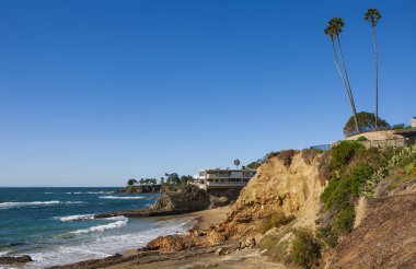 Bulutsuz bir günde San Clemente rıhtımının manzarası kayalık plajlar, yüksek palmiye ağaçları ve pahalı sahil manzaralı gayrimenkul.. 