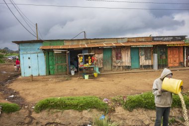 Migori, Kenya, - 21 Haziran 2025: Çalışan ve yaşayan insanların toprak yollarından görülen şehir hayatı. Yetişkinler bulutlu bir günde meyve ve sebze satan tezgahların önünden geçiyor..