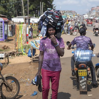 Migori, Kenya, - 21 Haziran 2025: Çalışan ve yaşayan insanların toprak yollarından görülen şehir hayatı. Kafasında bir tomar çorap taşıyan bir adam işlek bir sokakta yürür ve mallarını satar..