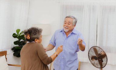 Asyalı, mutlu, emekli, yaşlı, gülümseyen, sevimli bir çift evde dans etmekten zevk alıyor. Emeklilikten sonra mutlu bir yaşam tarzı olan güzel bir evlilik aşığının romantik ilişkisi
