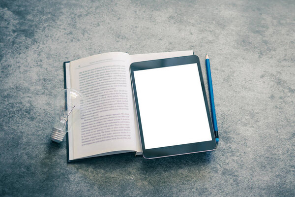 Blank screen tablet with textbook ,notebook, pencil and light bulb with copy space. Education concept of business studying, online learning course, or e-learning. Working at home via webinar.