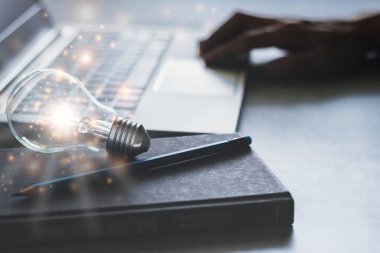 Parlayan ampullü ve ders kitaplı bir dizüstü bilgisayar. Kendi kendine öğrenme ya da eğitim bilgisi ve iş eğitimi kavramı. İnternetten veya evden öğrenme fikri.