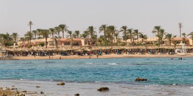 Hurghada, Egypt - September 29 2020: Beach with palms tree in Hurghada, tourists with sunbeds and umbrellas on the hot summer day.