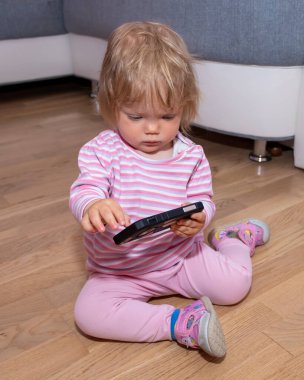 Evdeki küçük kız oynuyor ve cep telefonuna dokunuyor. Aletlere bebek bağımlılığı